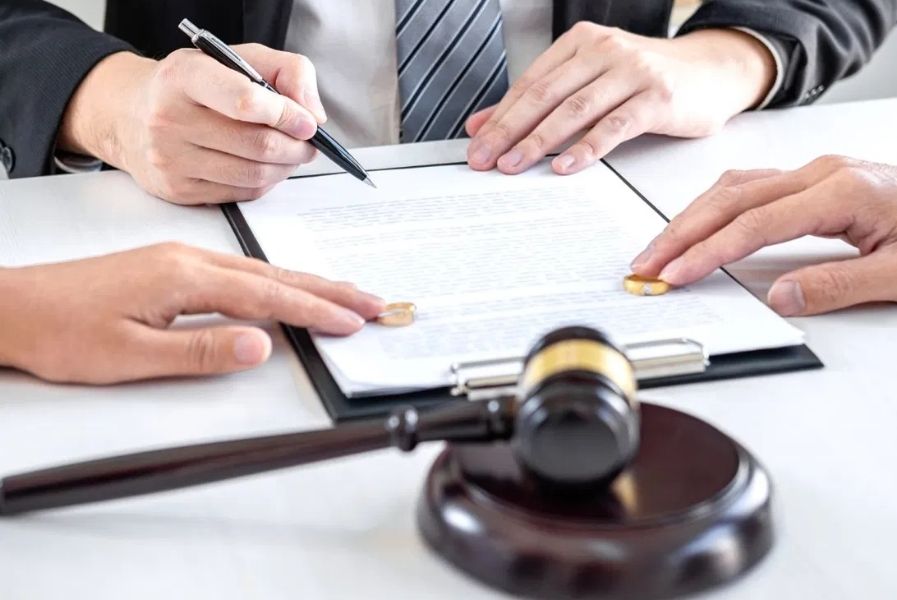 Attorney signing collaborative divorce agreement beside wedding rings and gavel